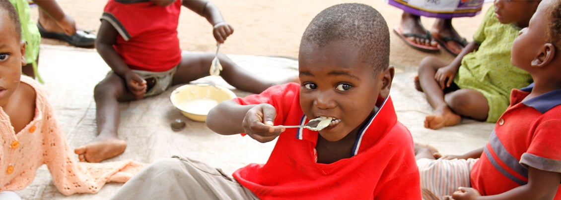 a small African boy sits on the ground eating porridge